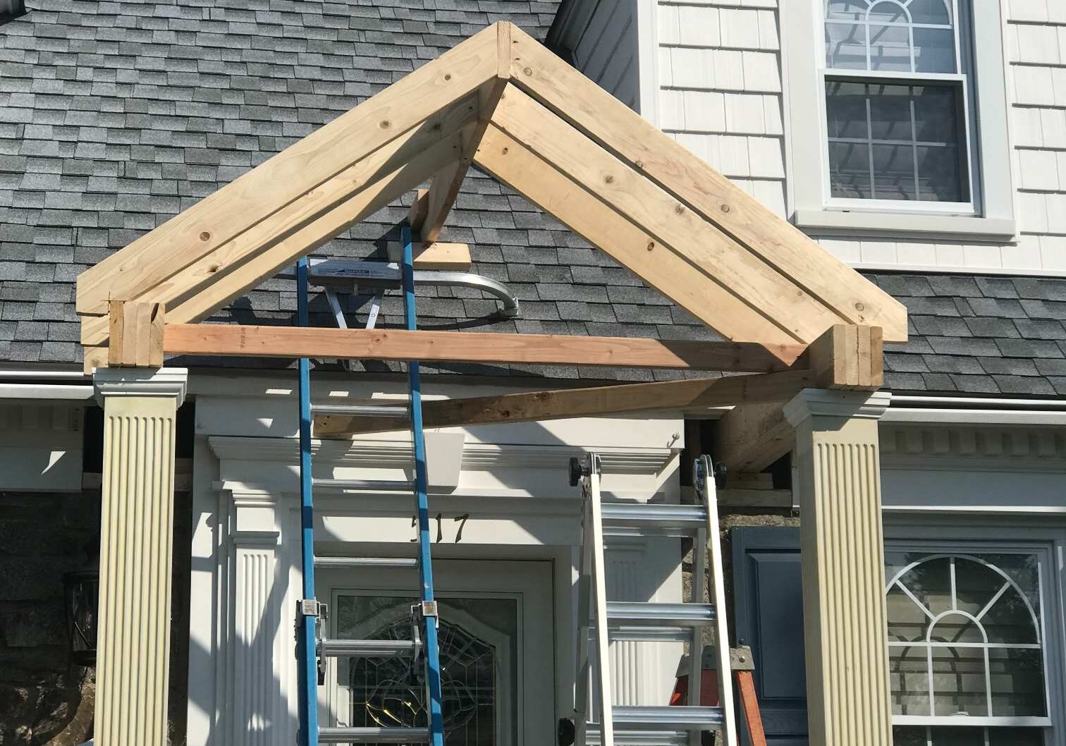 Construction of a wooden porch roof frame on a house.
